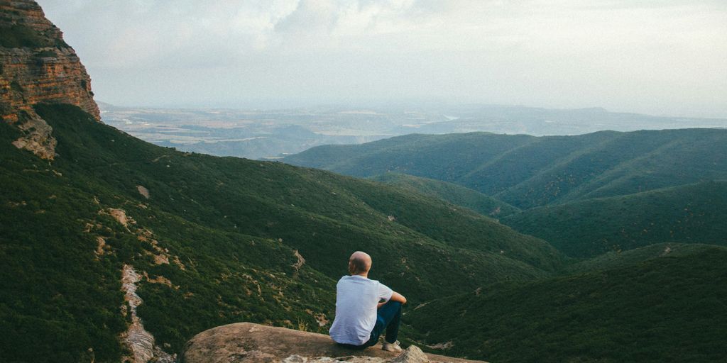 person sitting on the edge of a cliff over looking mountains during daytime