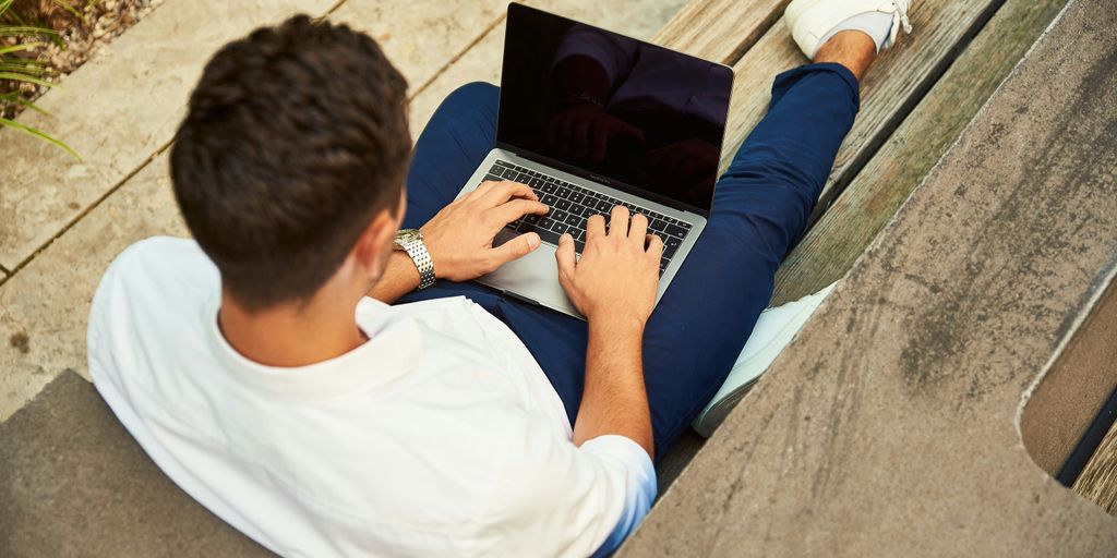 man wearing white sweatshirt using laptop computer sitting on sofa chair