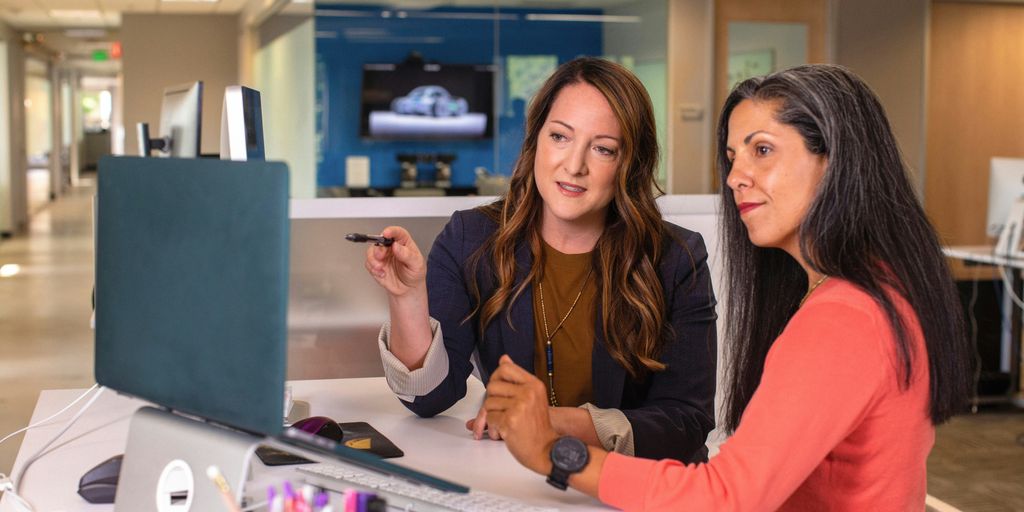 two women sitting at a table looking at a computer screen